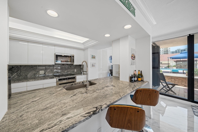 kitchen featuring appliances with stainless steel finishes, sink, white cabinets, ornamental molding, and light stone countertops