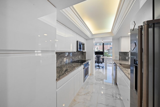 kitchen with stainless steel appliances, a tray ceiling, ornamental molding, white cabinets, and dark stone counters