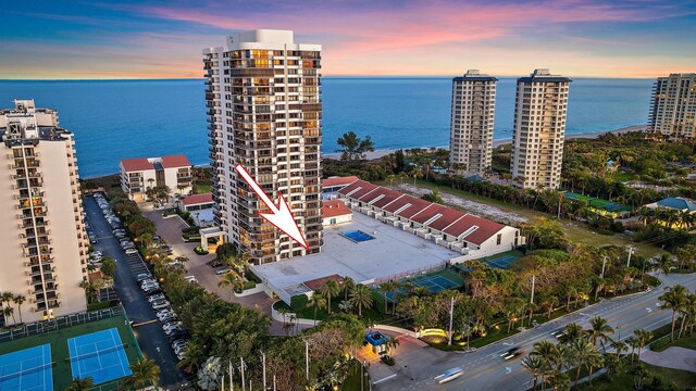 aerial view at dusk featuring a water view and a view of the beach