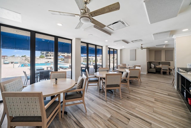 dining room with ceiling fan, a wall of windows, and light hardwood / wood-style floors