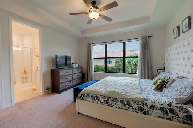 bedroom with ceiling fan, ensuite bath, a tray ceiling, and carpet floors