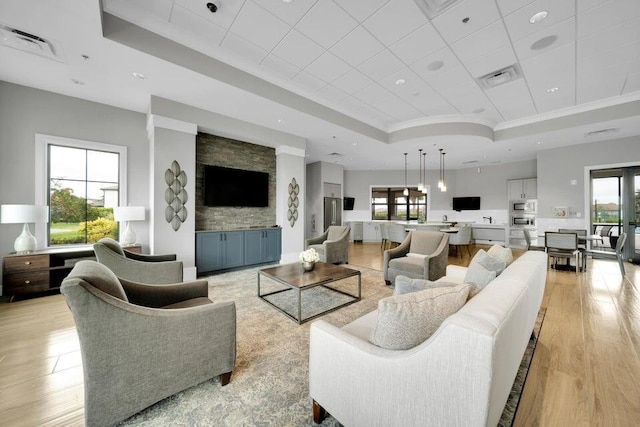 living room featuring a raised ceiling, ornamental molding, and light hardwood / wood-style flooring