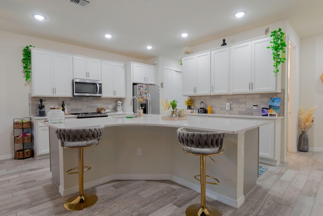 kitchen with appliances with stainless steel finishes, a kitchen island with sink, a breakfast bar area, and white cabinets