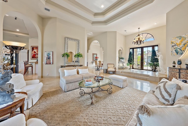 living room with french doors, crown molding, an inviting chandelier, a raised ceiling, and a towering ceiling