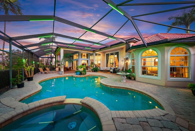 pool at dusk with an in ground hot tub, a patio area, and glass enclosure