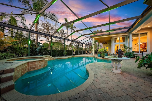 pool at dusk with ceiling fan, a patio area, glass enclosure, and an in ground hot tub