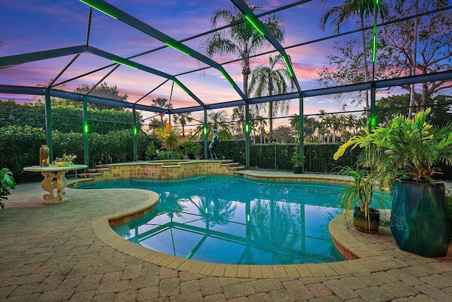 pool at dusk featuring a lanai, a patio, and an in ground hot tub