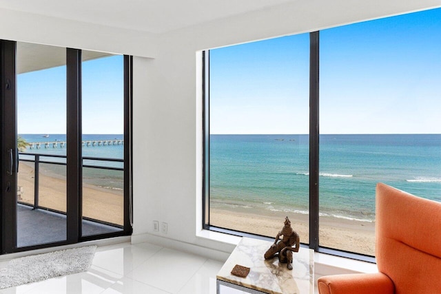 unfurnished living room with tile patterned floors, a water view, and a view of the beach