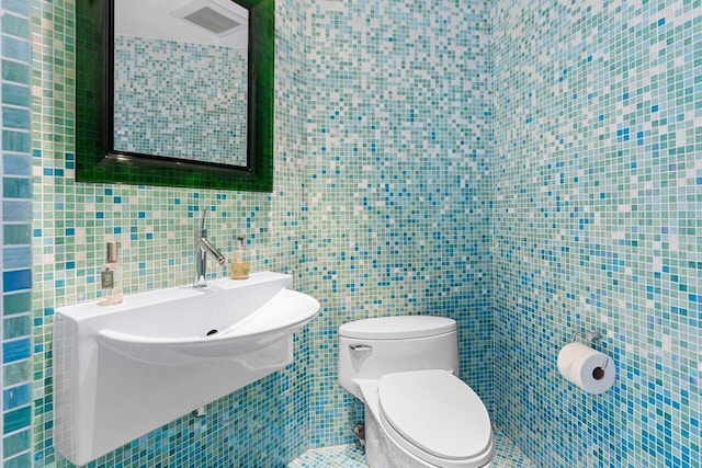 half bath with visible vents, toilet, and tile walls