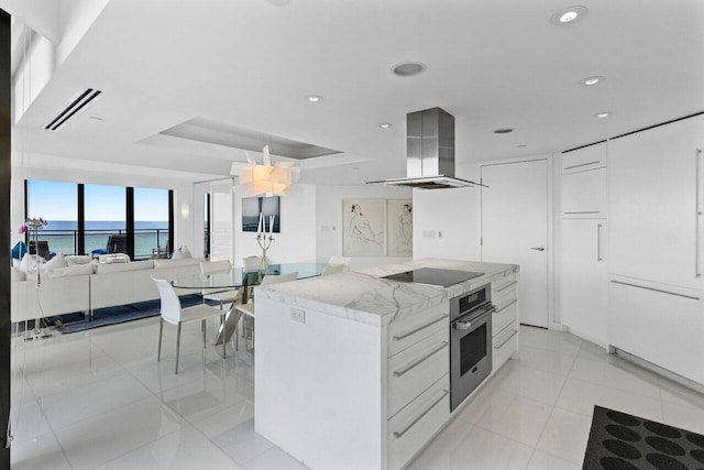 kitchen featuring island range hood, white cabinetry, oven, black electric stovetop, and a water view