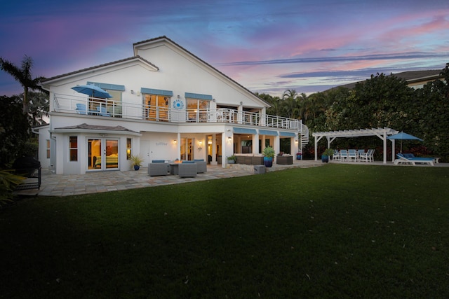 back house at dusk with a pergola, a patio, outdoor lounge area, a balcony, and a yard