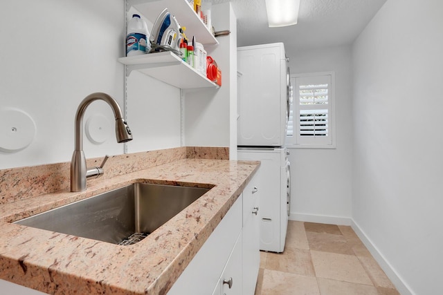 kitchen with light stone counters, sink, white cabinets, and stacked washing maching and dryer