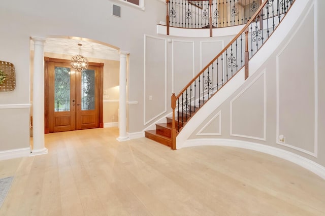 entrance foyer with a notable chandelier, a high ceiling, ornate columns, and wood-type flooring