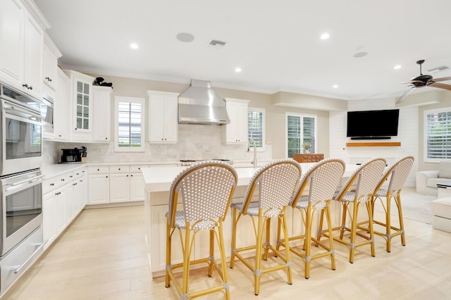 kitchen with a kitchen breakfast bar, white cabinets, wall chimney range hood, and ornamental molding