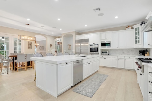 kitchen with decorative light fixtures, sink, backsplash, a center island with sink, and built in appliances