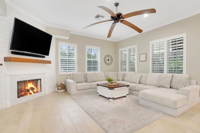 living room featuring light hardwood / wood-style floors, a large fireplace, crown molding, and ceiling fan