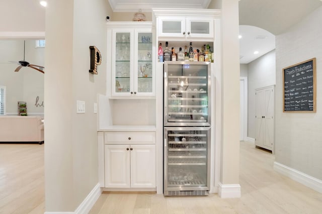 bar with light hardwood / wood-style floors, white cabinets, ornamental molding, and wine cooler