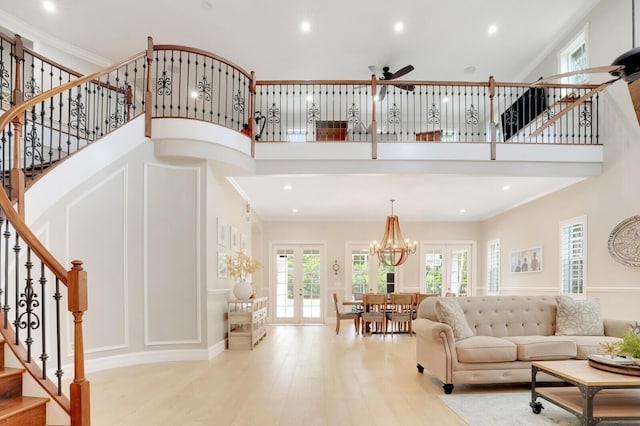 living room with light hardwood / wood-style flooring, french doors, a high ceiling, ceiling fan with notable chandelier, and ornamental molding