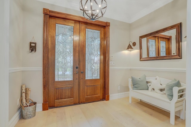 foyer featuring a chandelier, wood-type flooring, crown molding, and french doors