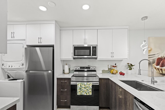 kitchen featuring stacked washer / drying machine, sink, hanging light fixtures, stainless steel appliances, and white cabinets