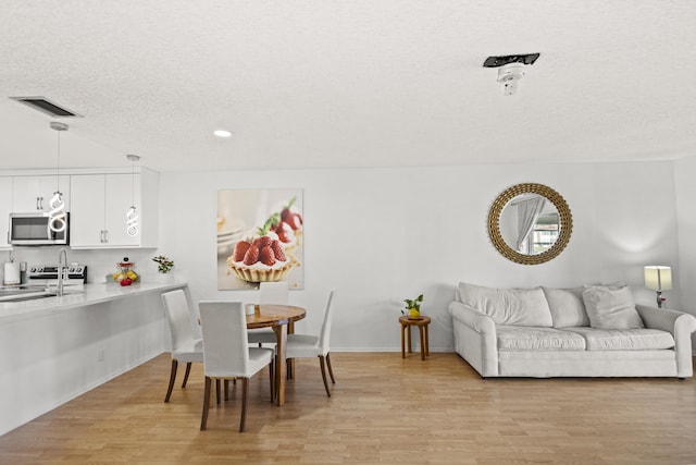 dining room featuring sink, a textured ceiling, and light wood-type flooring