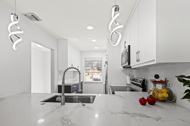 kitchen with light stone counters, appliances with stainless steel finishes, hanging light fixtures, and white cabinets