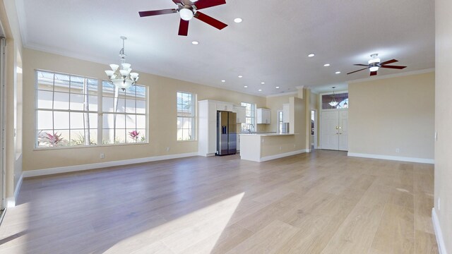 unfurnished living room featuring ornamental molding, ceiling fan with notable chandelier, and light hardwood / wood-style floors