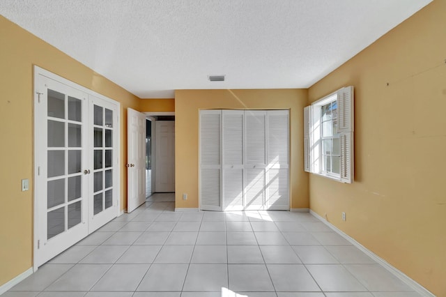 unfurnished bedroom with a closet, light tile patterned floors, a textured ceiling, and french doors