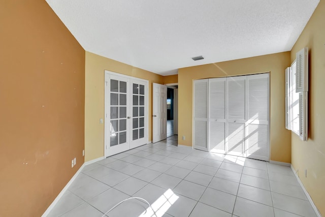 unfurnished bedroom with a closet, french doors, a textured ceiling, and light tile patterned flooring