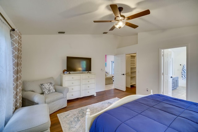 bedroom featuring a spacious closet, visible vents, vaulted ceiling, and wood finished floors