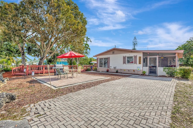 rear view of house featuring a wooden deck, a sunroom, and a patio area