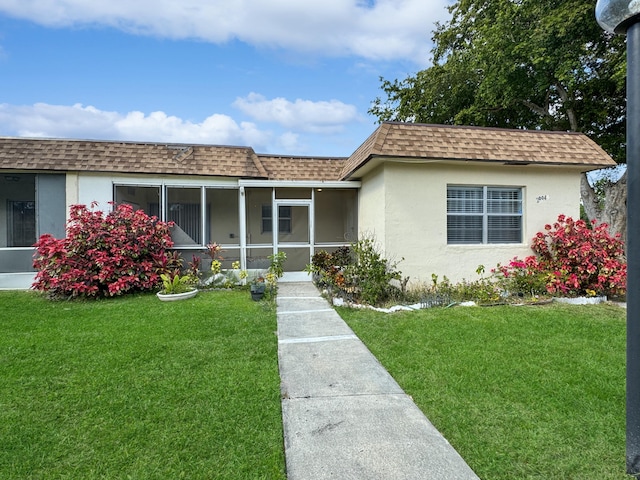 single story home featuring a front yard, roof with shingles, stucco siding, mansard roof, and a sunroom