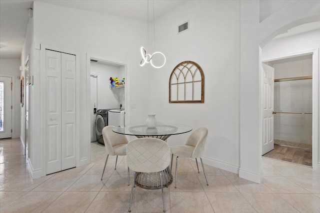 tiled dining space featuring an inviting chandelier, washer and clothes dryer, and a high ceiling