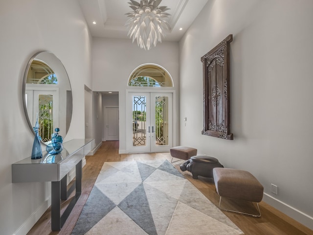 foyer entrance featuring light wood-type flooring, a towering ceiling, french doors, and a chandelier