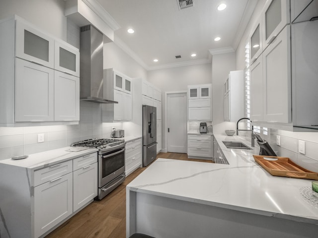 kitchen with wall chimney exhaust hood, white cabinetry, appliances with stainless steel finishes, and sink