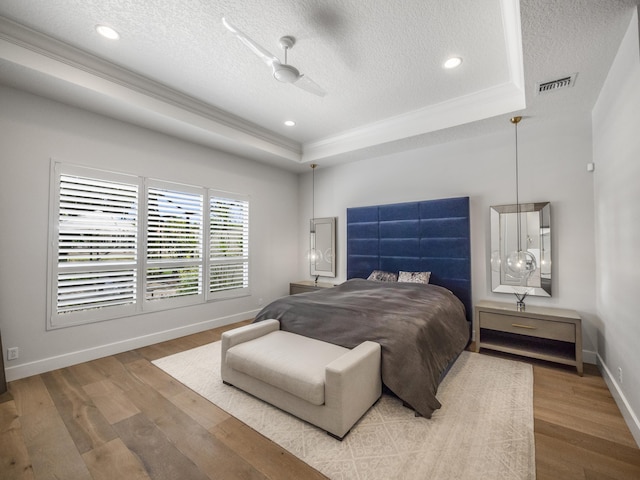 bedroom with hardwood / wood-style floors, a textured ceiling, ceiling fan, and a raised ceiling