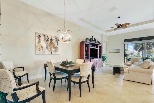 dining area with ceiling fan with notable chandelier and a tray ceiling