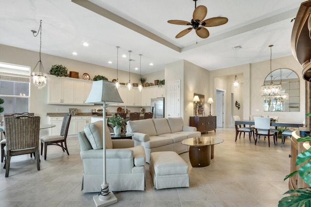 tiled living room with ceiling fan with notable chandelier and a tray ceiling