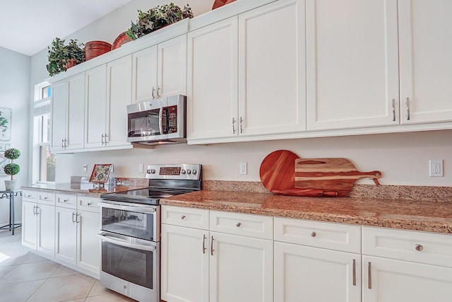 kitchen with light stone countertops, light tile patterned flooring, white cabinets, and appliances with stainless steel finishes