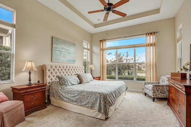 bedroom with light carpet, a raised ceiling, and ceiling fan