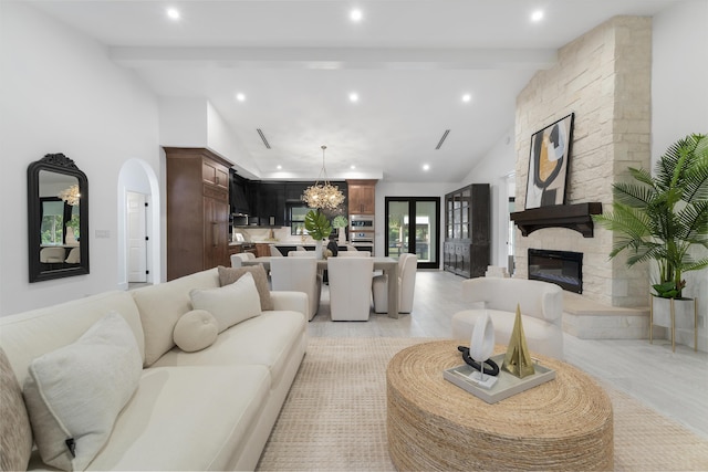 living room with light hardwood / wood-style floors, a notable chandelier, a stone fireplace, and vaulted ceiling with beams