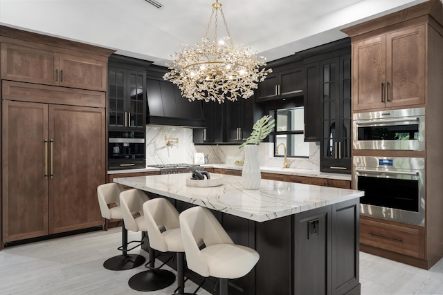 kitchen with appliances with stainless steel finishes, a kitchen island, hanging light fixtures, light stone counters, and custom range hood