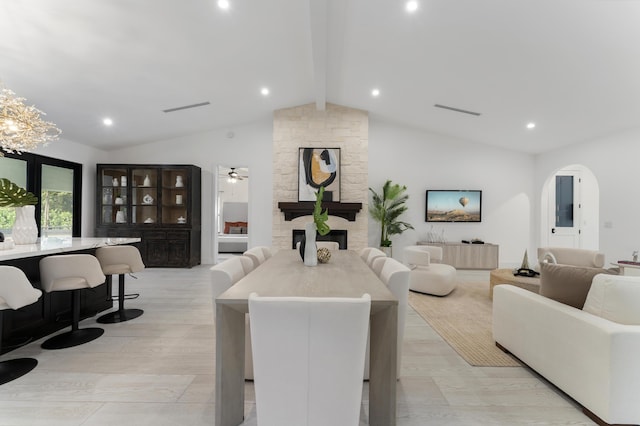 living room featuring ceiling fan, vaulted ceiling with beams, and a stone fireplace