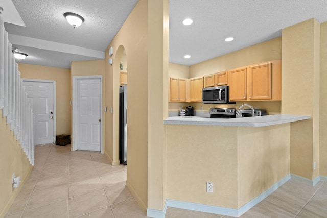 kitchen featuring light brown cabinetry, a textured ceiling, light tile patterned floors, kitchen peninsula, and stainless steel appliances