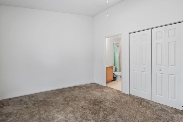 unfurnished bedroom featuring a closet, ensuite bathroom, and light colored carpet