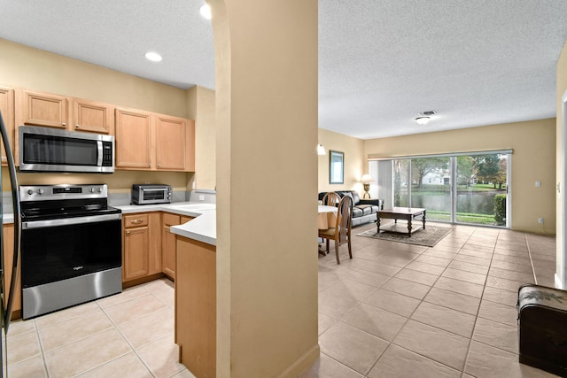 kitchen with light brown cabinets, a textured ceiling, light tile patterned floors, and stainless steel appliances