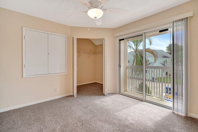 unfurnished bedroom featuring a walk in closet, carpet, access to exterior, a textured ceiling, and a closet