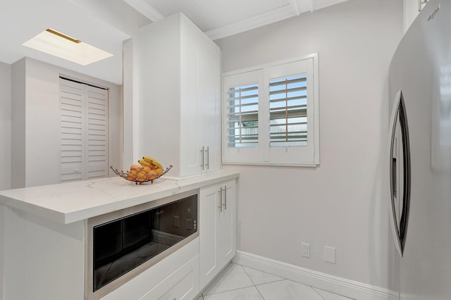 kitchen featuring kitchen peninsula, stainless steel fridge, white cabinets, light tile patterned floors, and light stone counters