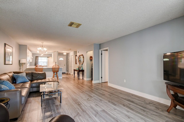 living room with light hardwood / wood-style floors, a textured ceiling, and an inviting chandelier