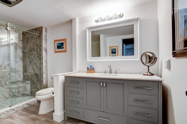 bathroom featuring hardwood / wood-style flooring, toilet, vanity, and a tile shower